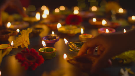 Nahaufnahme-Von-Händen,-Die-Diya-Öllampen-Anzünden,-Um-Das-Diwali-Fest-Auf-Abgedunkeltem-Tisch-Zu-Feiern-1
